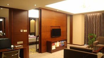 A hotel room with a TV, a desk, a chair, a sofa, a bookshelf, and a mirror.