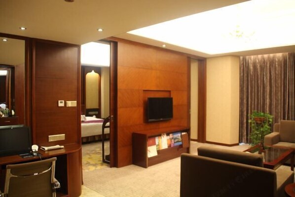 A hotel room with a TV, a desk, a chair, a sofa, a bookshelf, and a mirror. - Guowei Hotel (Menghai)