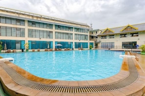 Une piscine dotée d’une terrasse ensoleillée, d’un espace salon couvert et d’un bâtiment aux grandes fenêtres.