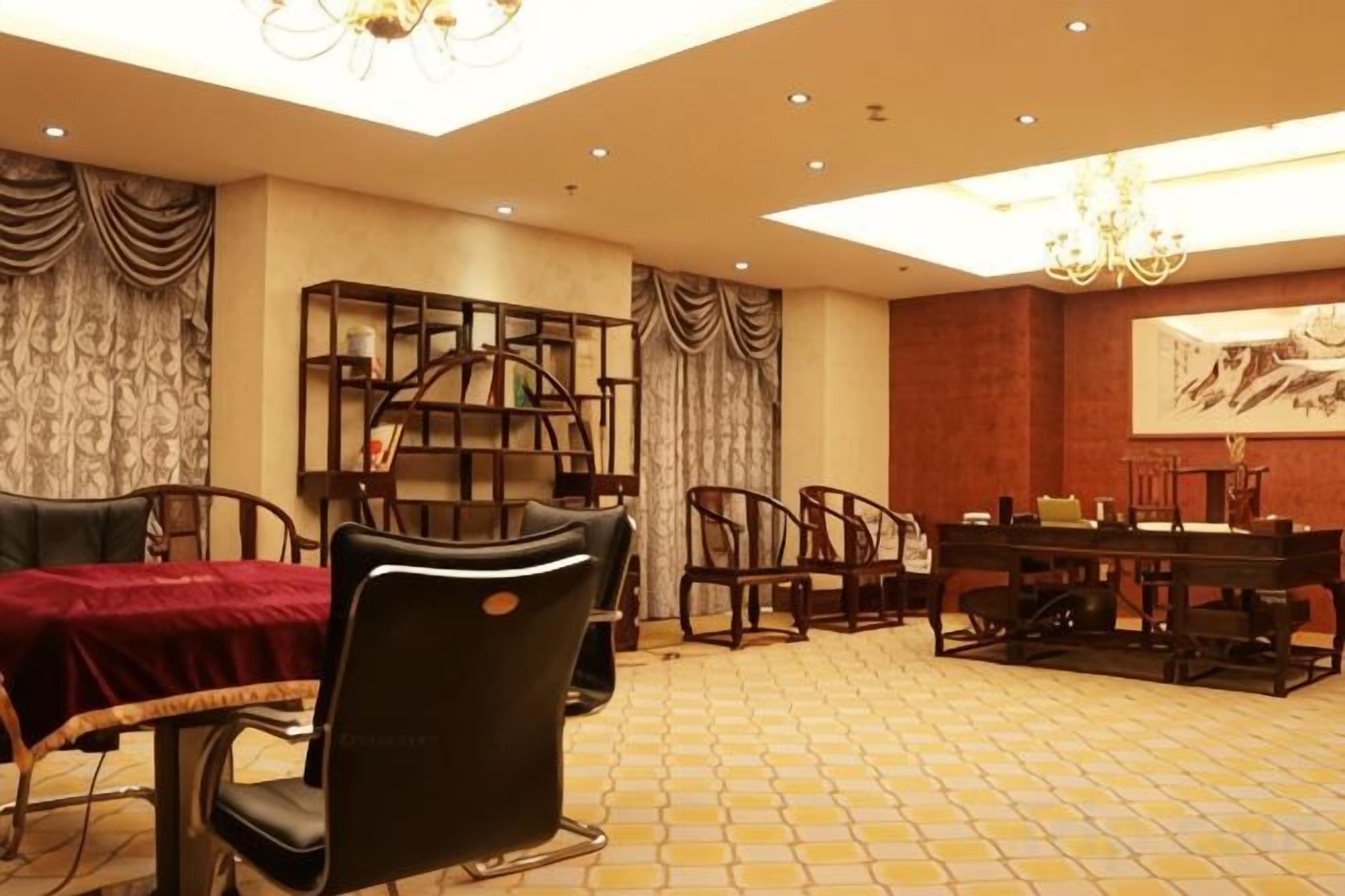 A hotel dining area with a red table, black chairs, a bookshelf, and a chandelier.