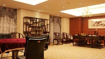 A hotel dining area with a red table, black chairs, a bookshelf, and a chandelier.