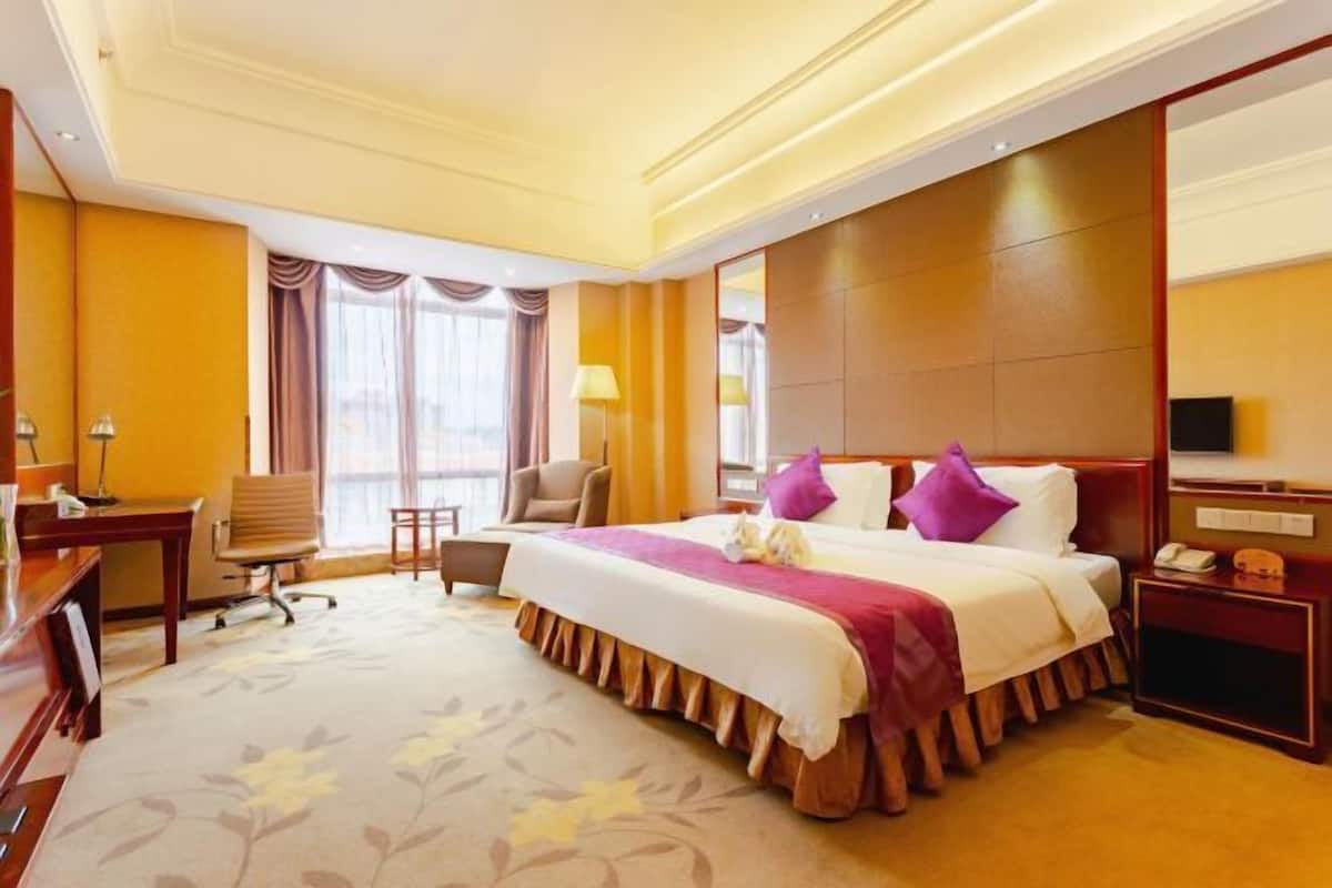 Una habitación de hotel con una cama grande, un escritorio, una silla, un televisor y una ventana con cortinas.