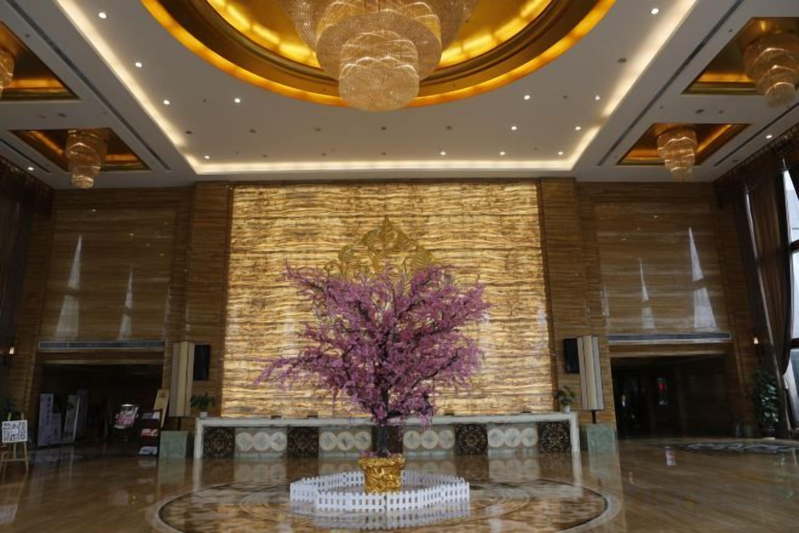 A lobby with a central reception desk, a large decorative wall, and a chandelier.