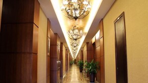 A hotel corridor with chandeliers, wooden paneling, and potted plants. - Guowei Hotel (Menghai)