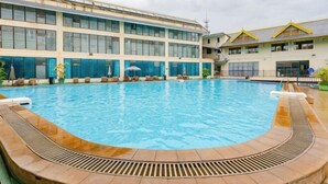 A swimming pool with a sun deck, a large building with multiple windows, and a clear sky. - Guowei Hotel (Menghai)
