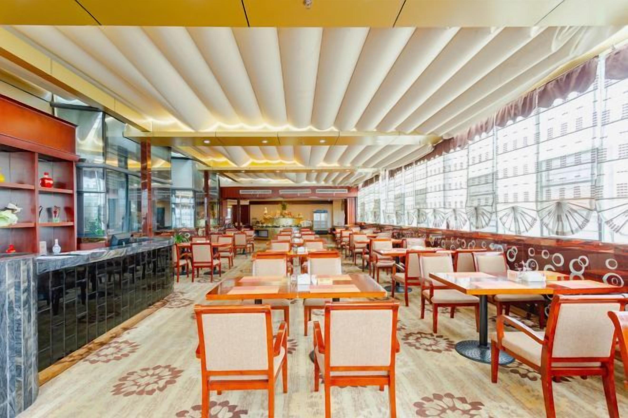 A restaurant with multiple dining tables and chairs, a bar area, and large windows.