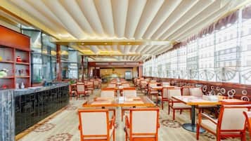 A restaurant with multiple dining tables and chairs, a bar area, and large windows.