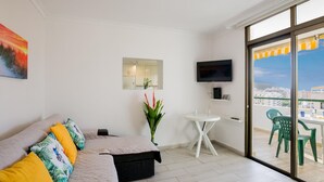 Ein modernes Wohnzimmer mit einer Couch, einem kleinen Tisch, einem Fernseher und einem Balkon mit Stühlen.