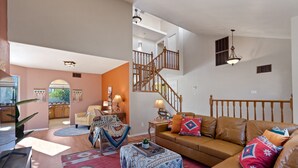 A spacious living room with a brown leather sofa, a patterned rug, and a staircase leading to an upper level. - Southwestern Paradise, Simply Classic (Oro Valley)