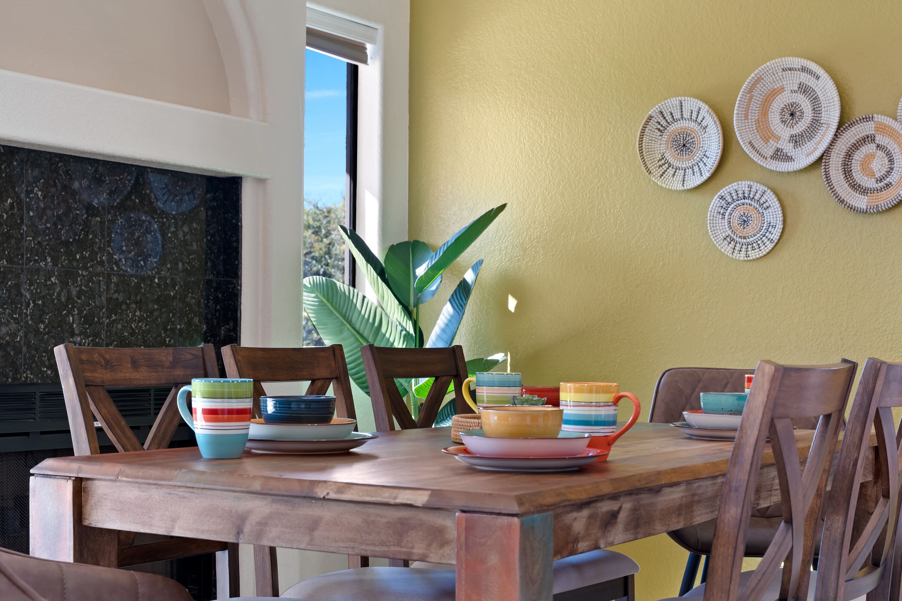 A dining area with a wooden table, chairs, and colorful dishes.