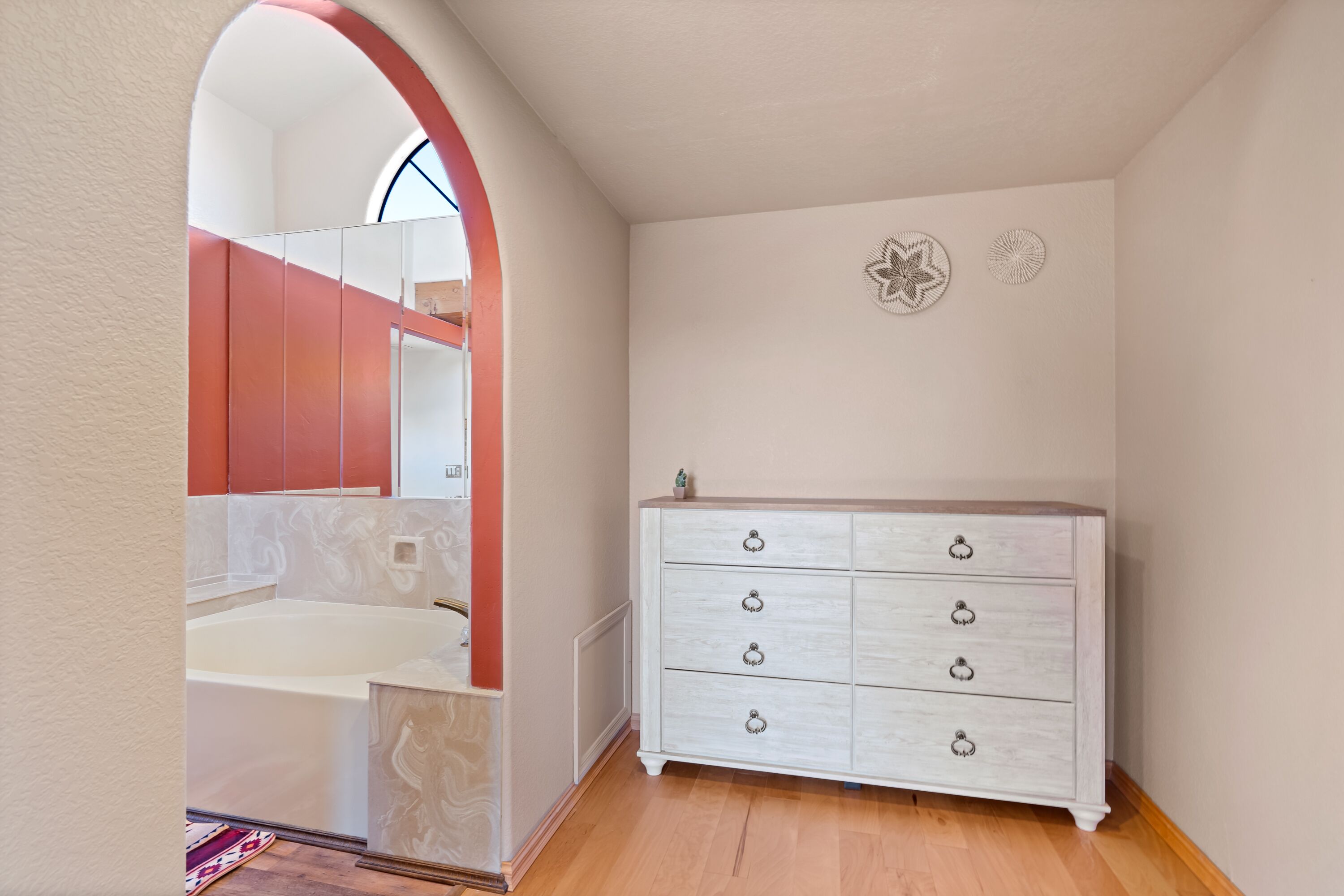Une salle de bain avec une baignoire, un meuble-lavabo avec un miroir et une commode blanche avec des tiroirs.