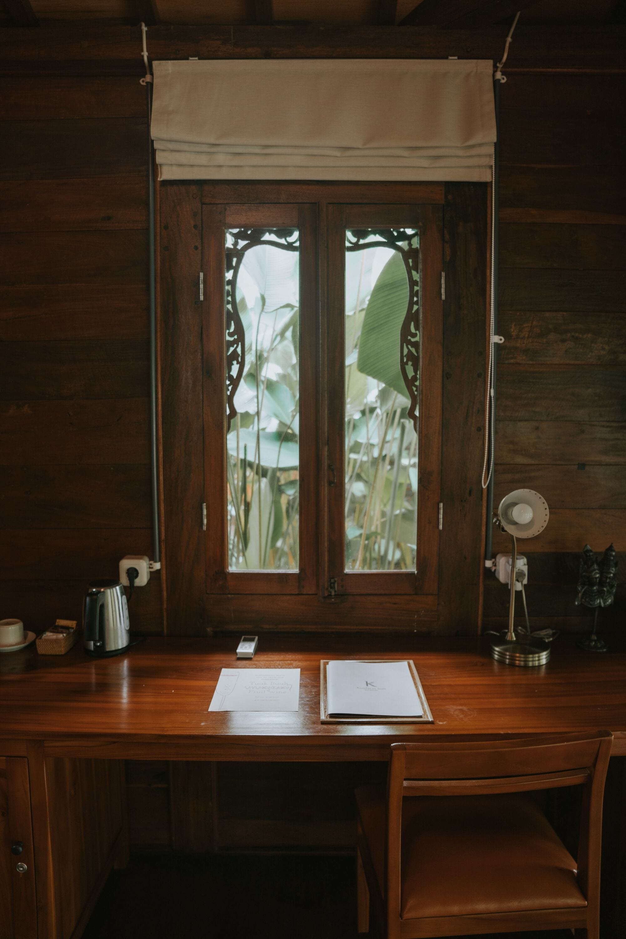 A wooden desk with a window, a kettle, a cup, and a notebook.