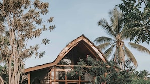 A wooden house with a porch, surrounded by a garden with rocks and plants. - Kusfarm Bali by AHM (Selemadeg)