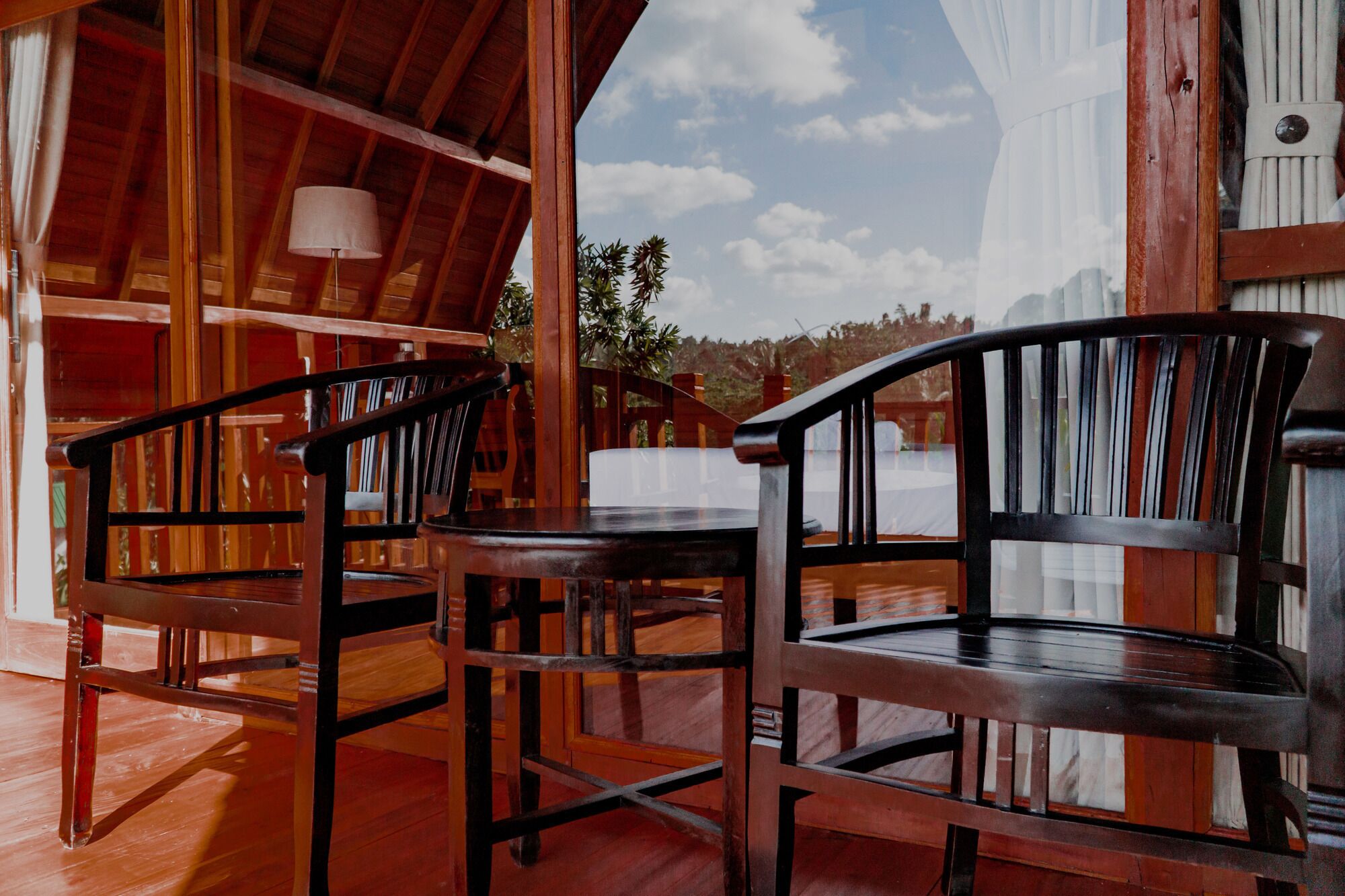 A wooden interior with two chairs and a table, a wooden ceiling, and a view of the outdoors.