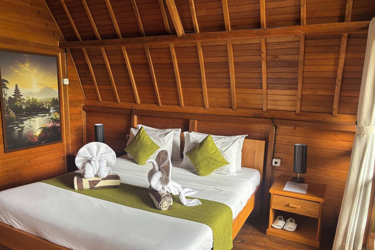A wooden room with a bed, pillows, a nightstand, and a painting.