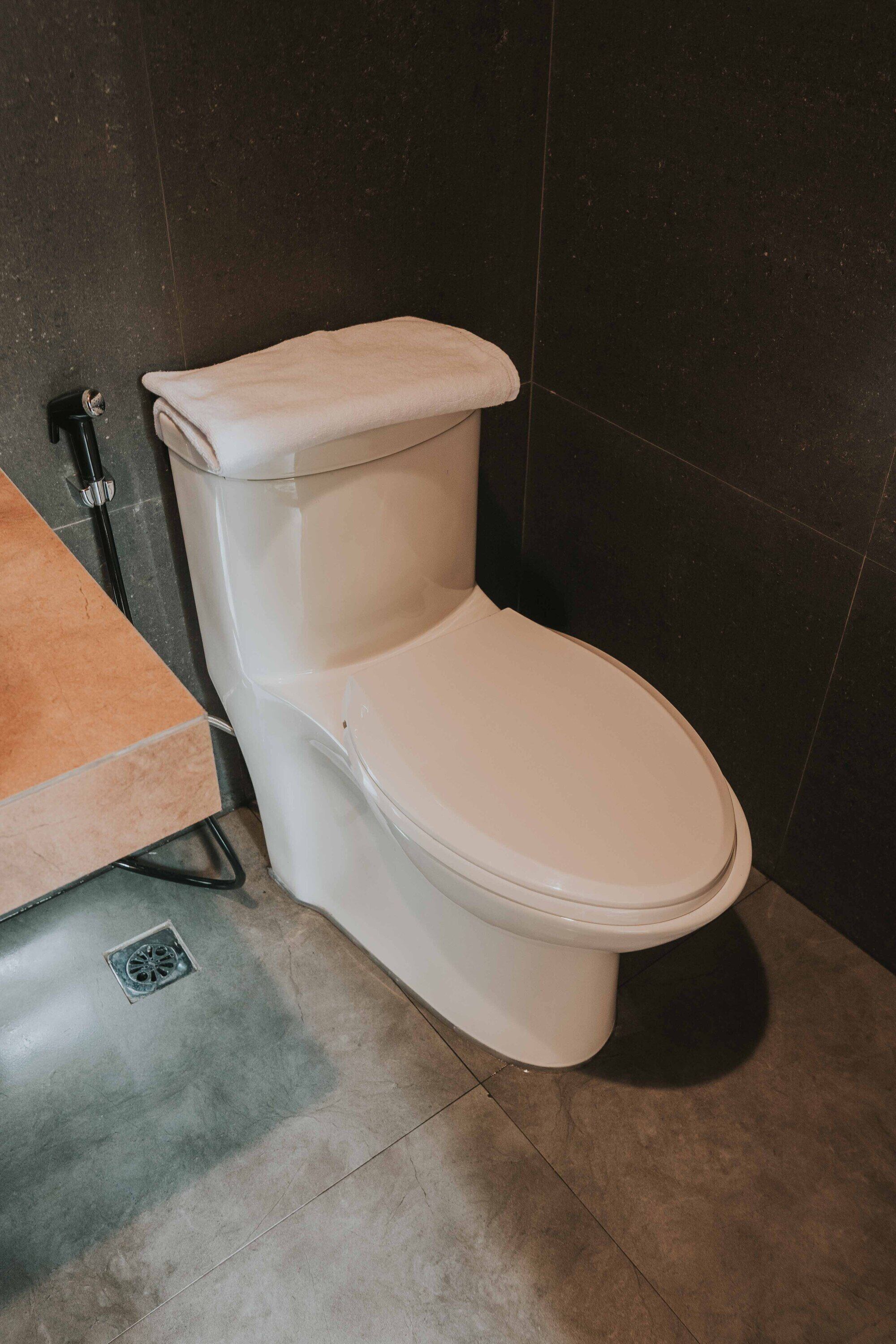Un inodoro con asiento y tanque blancos, desagüe visible y piso de baldosas.