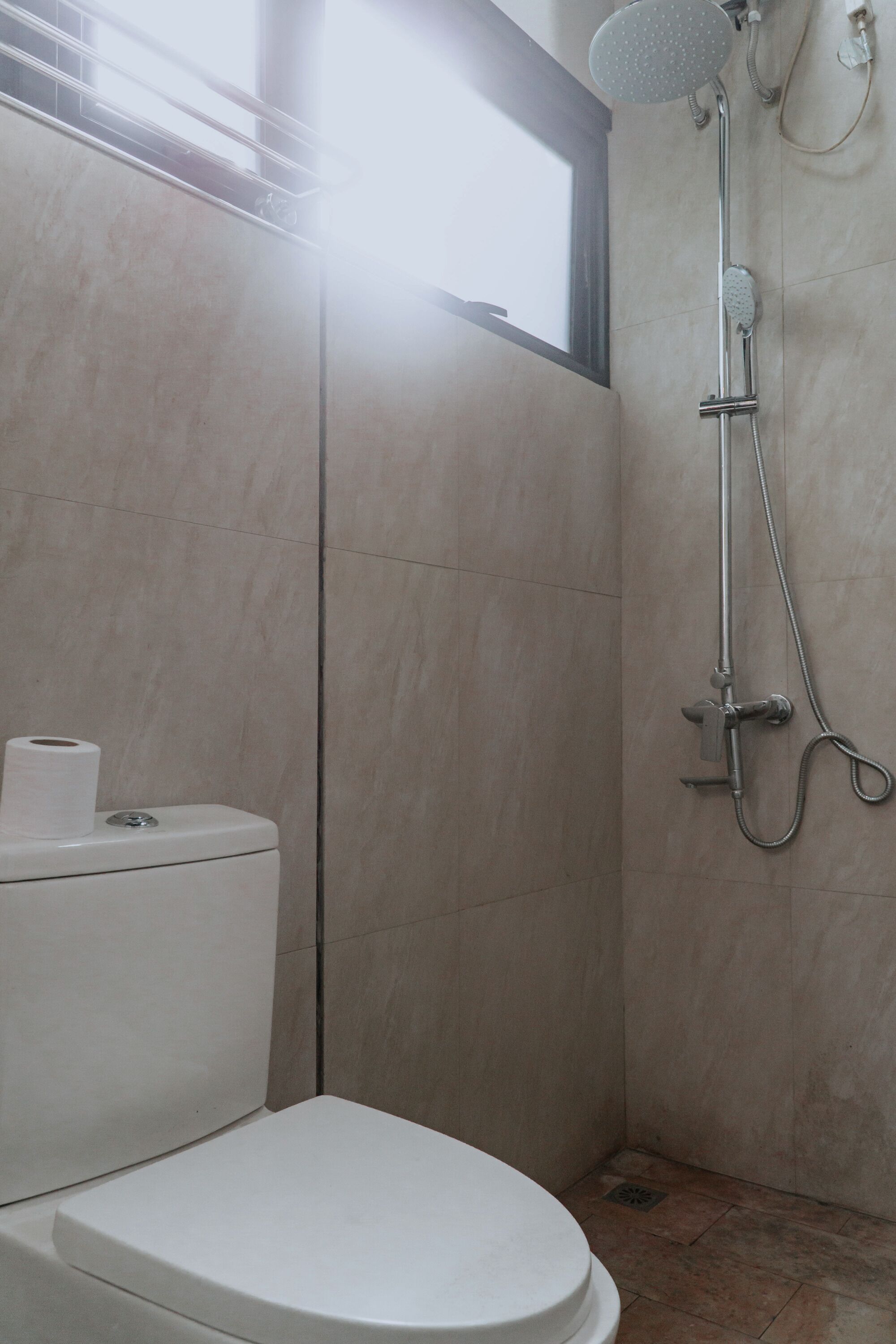 A bathroom with a toilet, a shower, and a window.