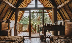 A cozy room with a wooden ceiling, a large sliding glass door leading to a balcony, and a small table with a lamp. - Kusfarm Bali by AHM (Selemadeg)