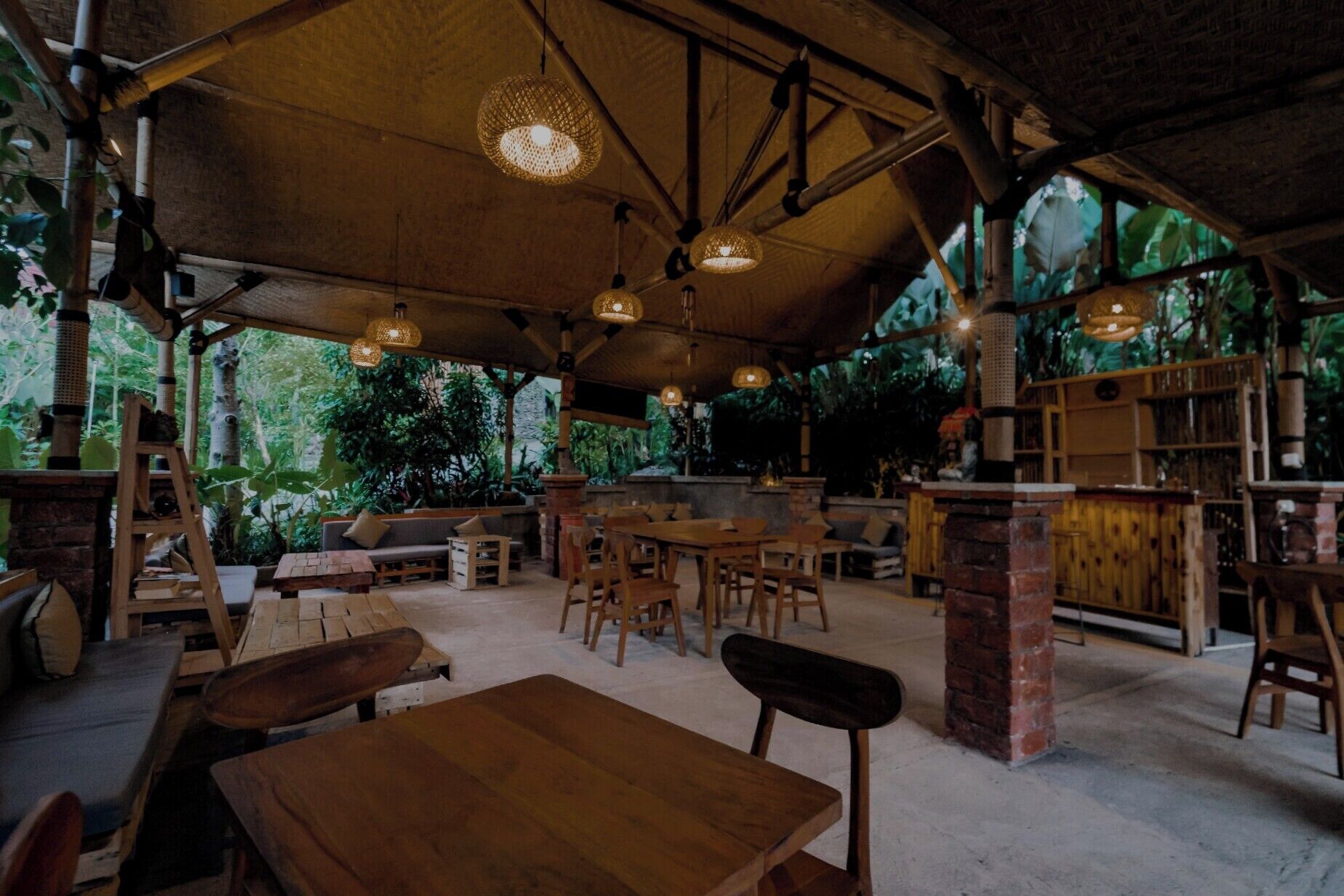An indoor dining area with wooden tables and chairs, a brick pillar, and hanging lights.
