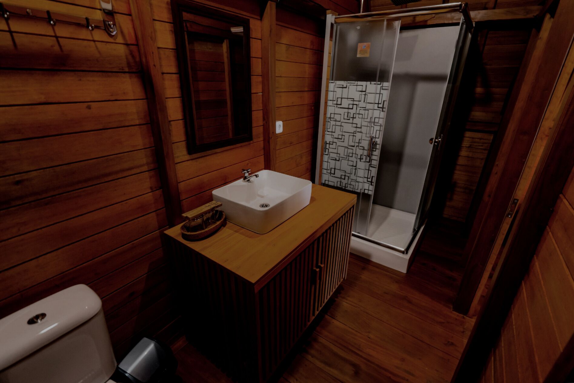 A wooden cabin bathroom with a white sink, a toilet, and a glass shower enclosure.