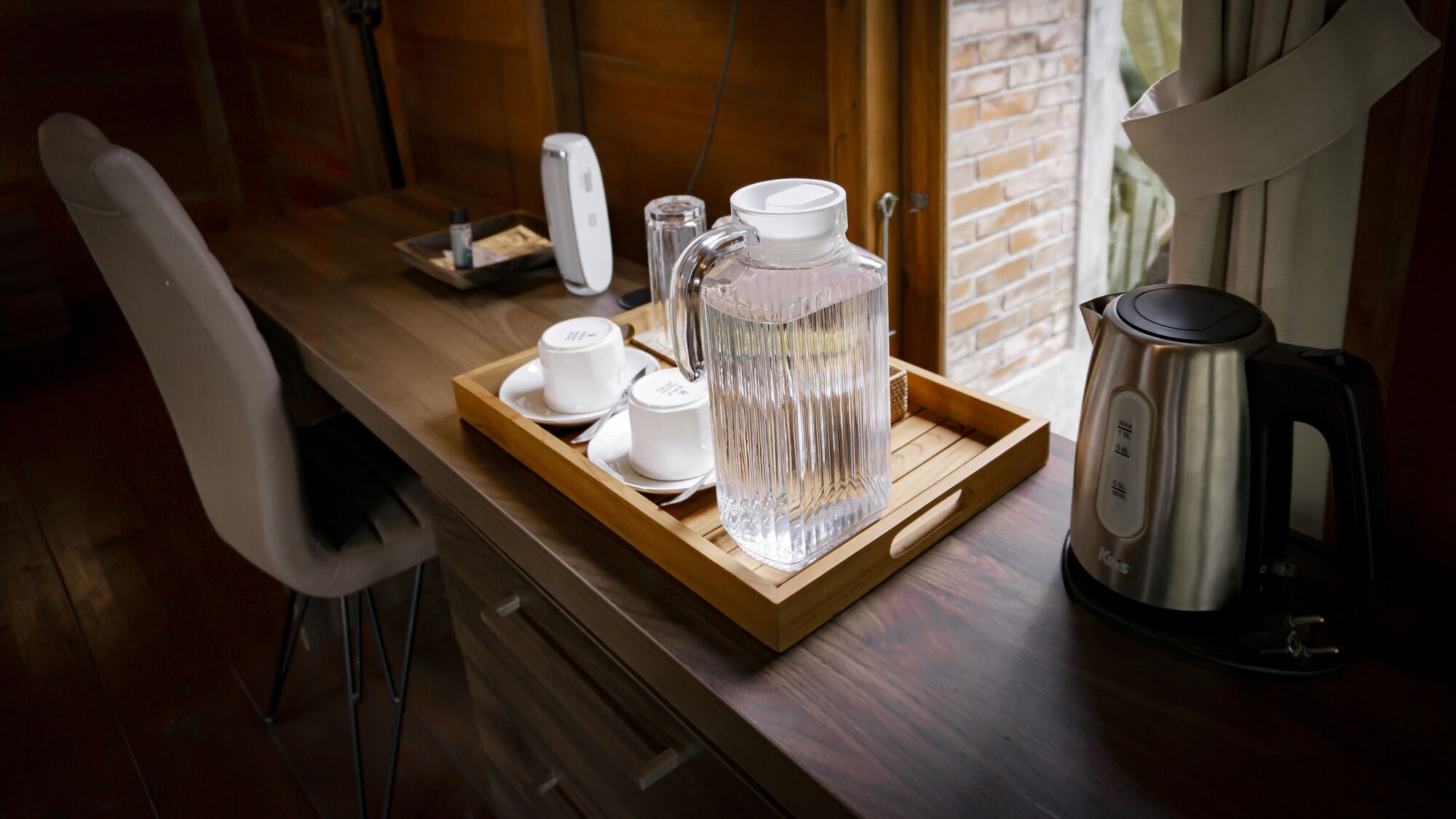 A wooden tray with a pitcher, cups, and a kettle on a kitchen counter.