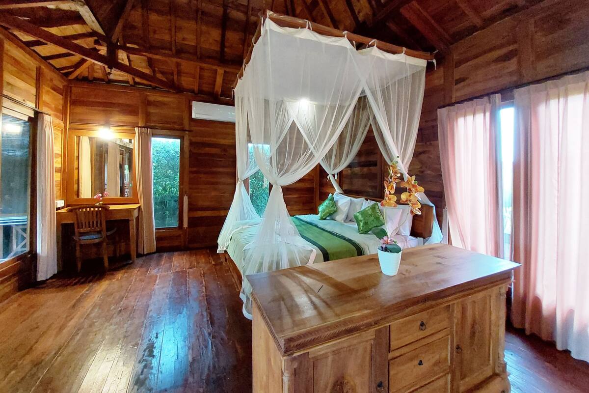 Ein Zimmer mit Holzboden und einem Bett unter einem Baldachin, einem Holztisch und einem Stuhl.