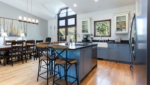 A modern kitchen with a central island, bar stools, a dining area with a table and chairs, and a view of the outdoors through large windows. - Steps From Slopes - Luxury Beaver Creek Townhome (Beaver Creek)