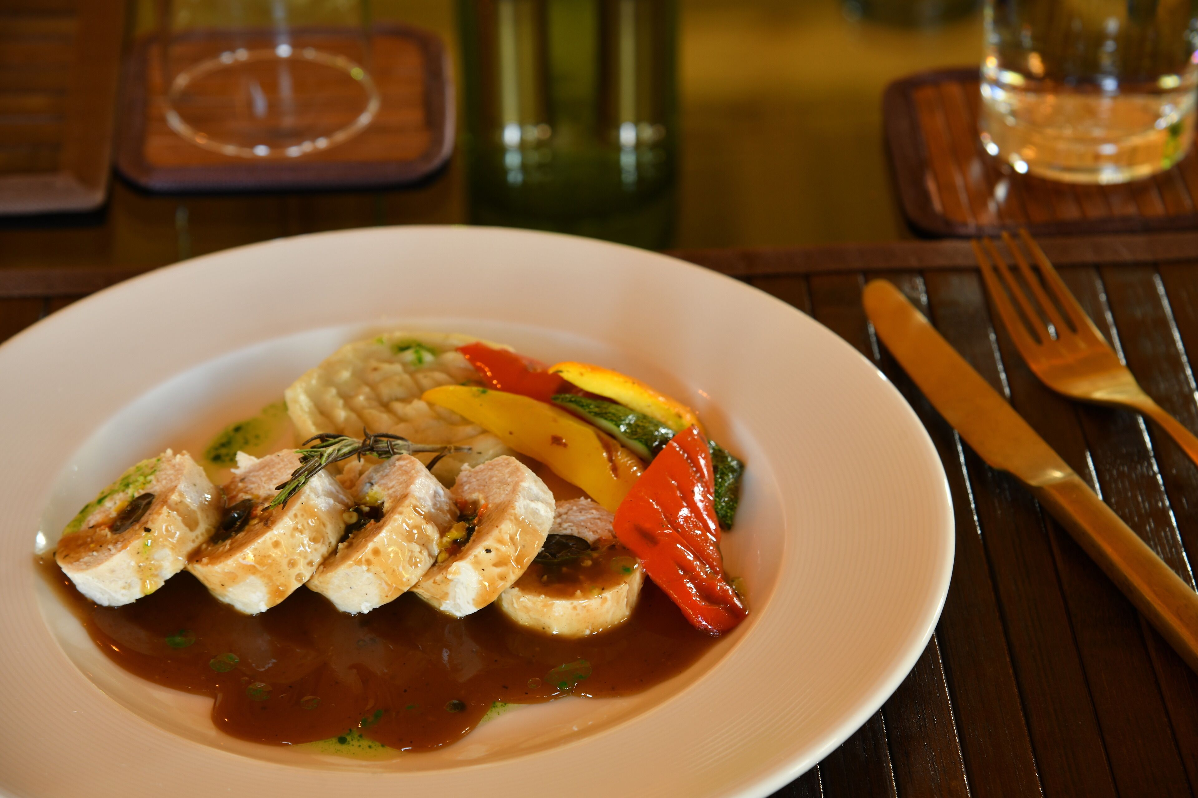 A plate of food with sliced meat, vegetables, and sauce on a wooden table.