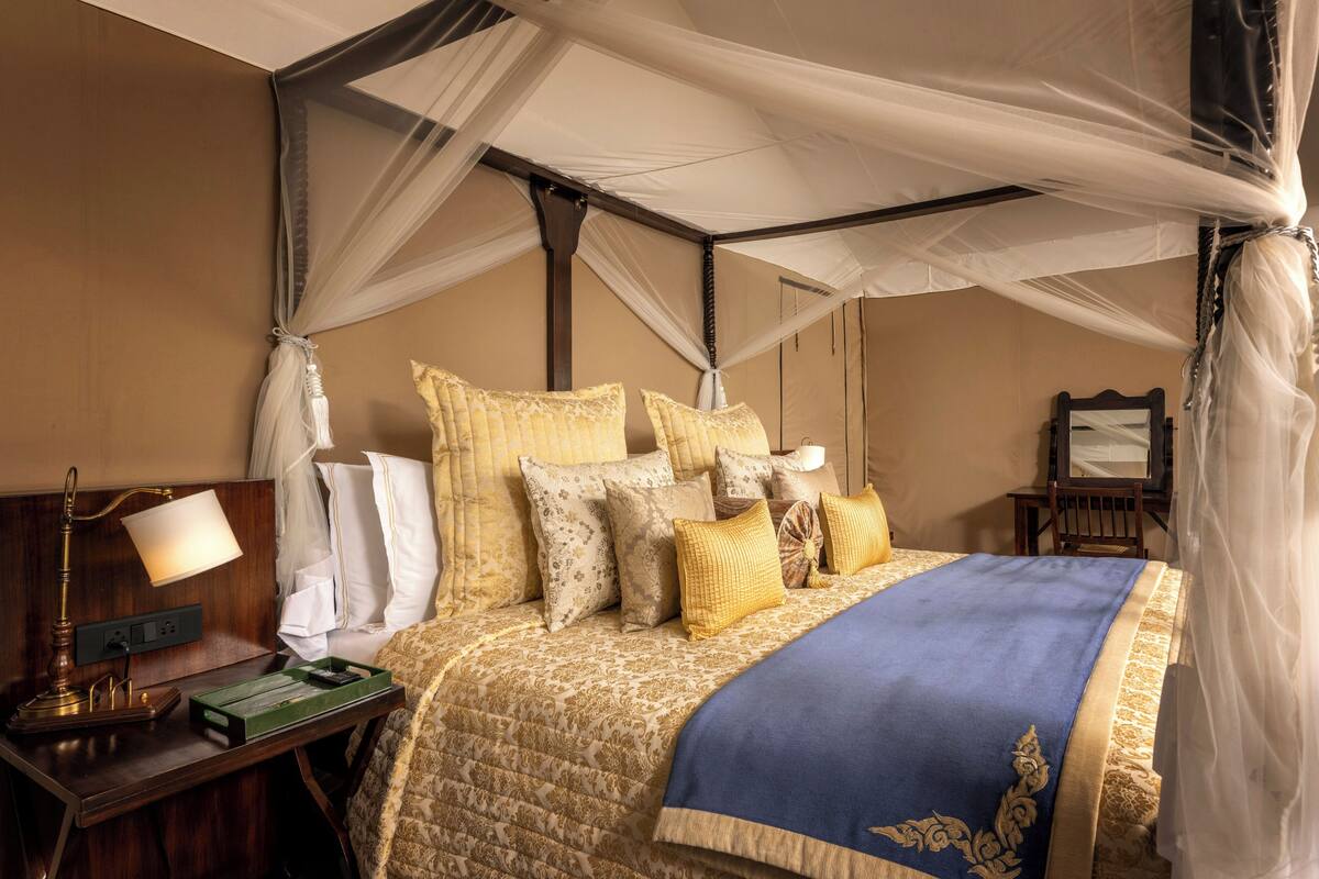 A bedroom with a canopy bed, bedside table with lamp, and a nightstand.