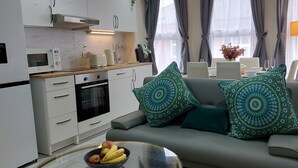 Ett modernt kök med mikrovågsugn, brödrost och vattenkokare, en matplats med bord och stolar samt ett vardagsrum med soffa och dekorativa kuddar.