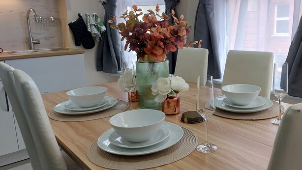 Ett matbord dukat med vita skålar och tallrikar, en vas med blommor och ett vinglas.