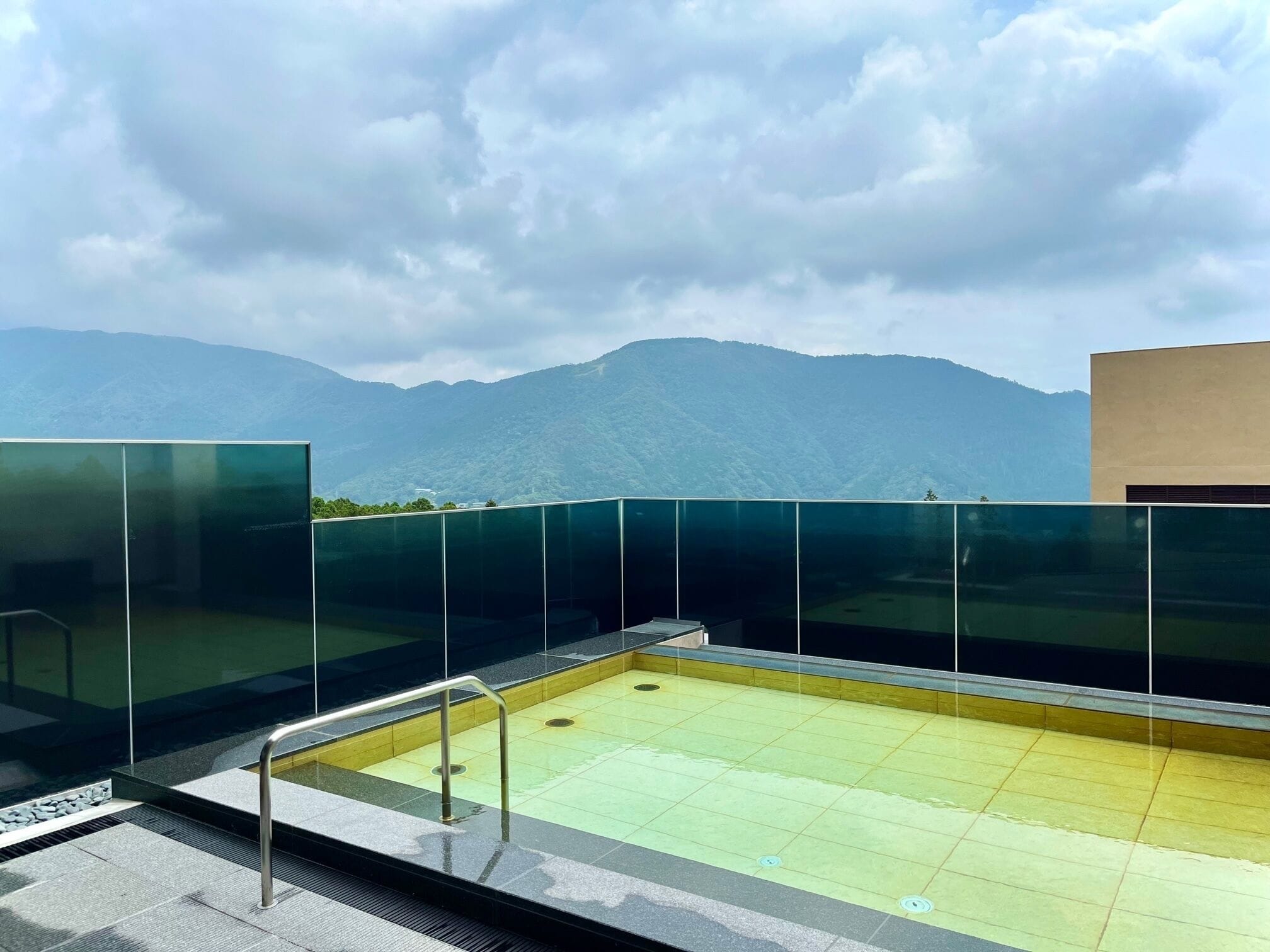 A rooftop pool with glass railings and a view of mountains.