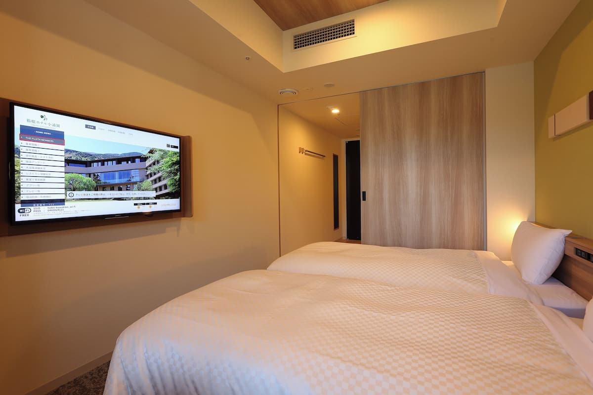 A hotel room with a bed, a television mounted on the wall, and a door leading to another room.
