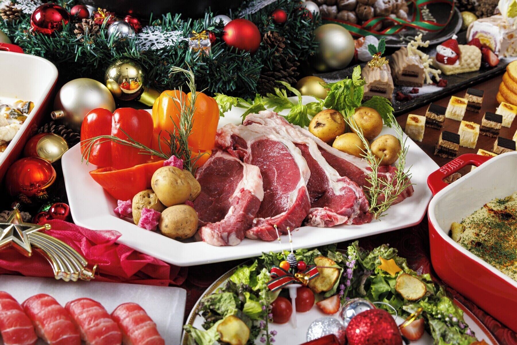 Una mesa festiva con una variedad de alimentos, incluyendo carne, papas y una ensalada, rodeada de adornos navideños.