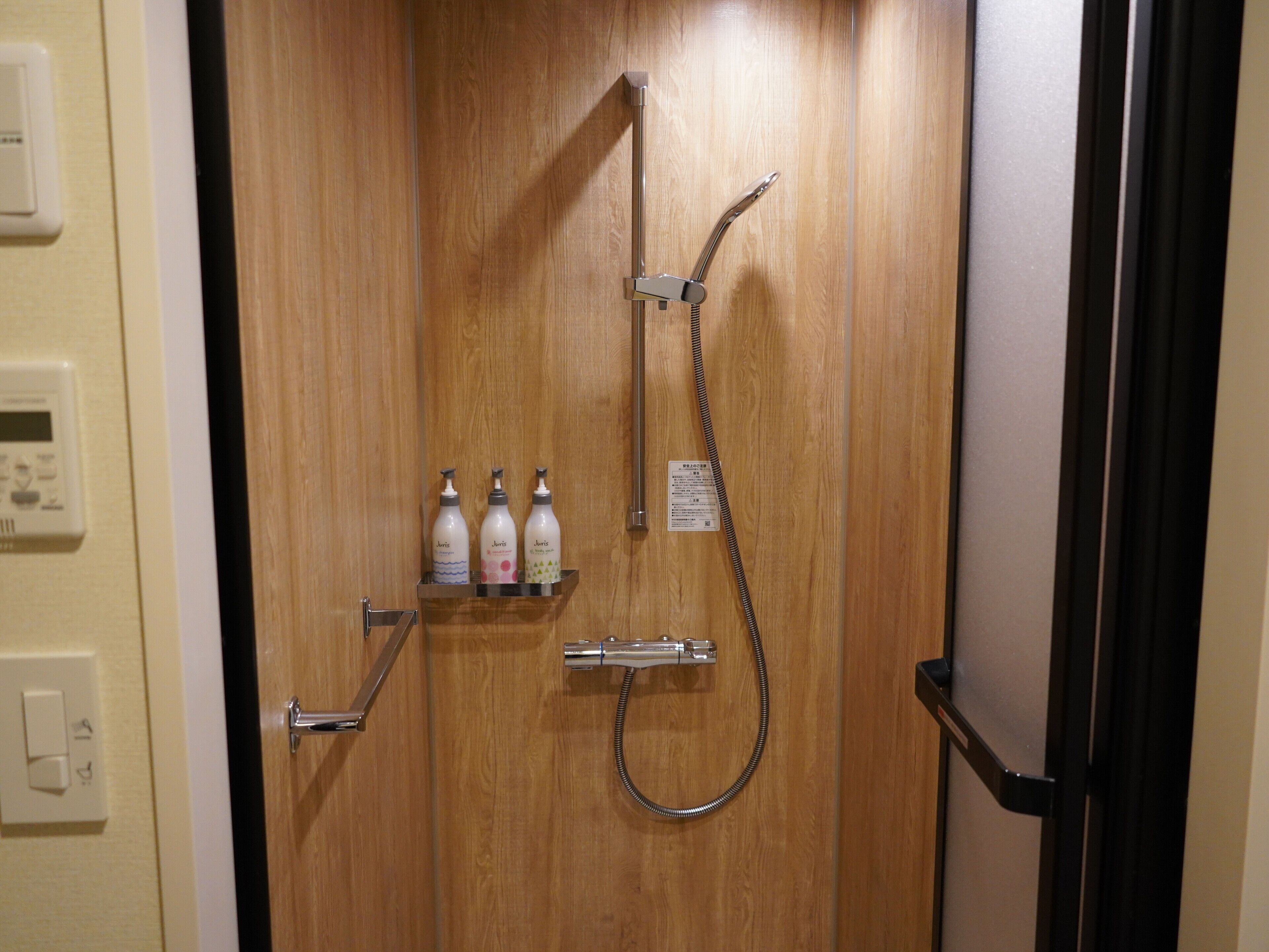 Una puerta de madera con ducha, un secamanos y tres botellas de champú.