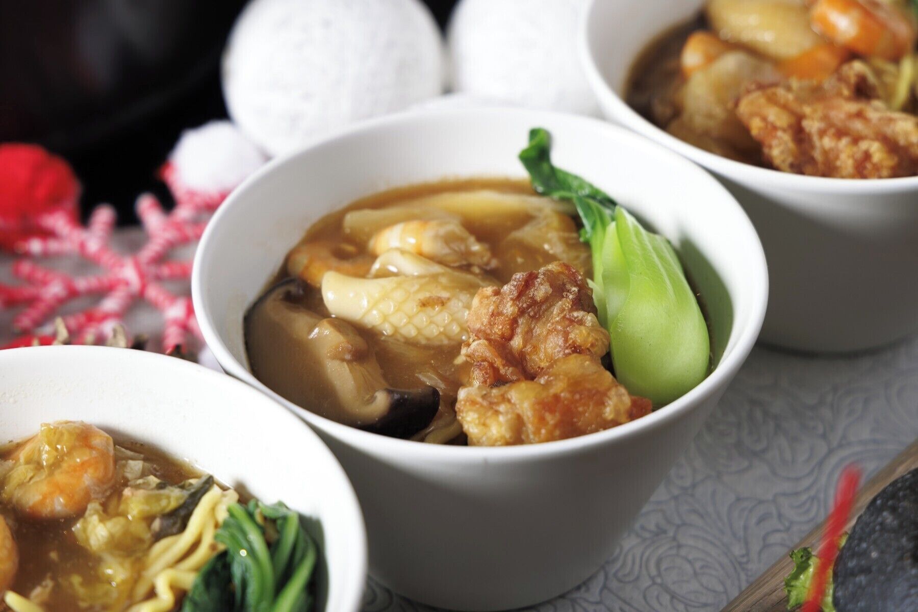 Three bowls of soup with various ingredients, including meat and vegetables, on a table.