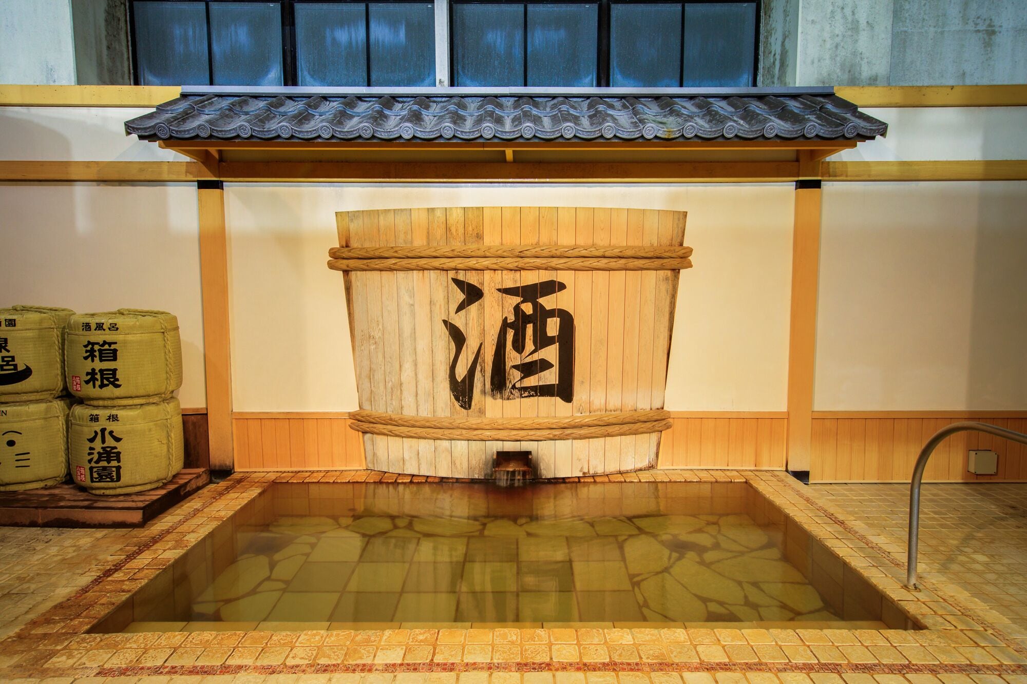 Un botlle de sake japonès tradicional amb una base de fusta i un teulat de rajoles a la part superior.