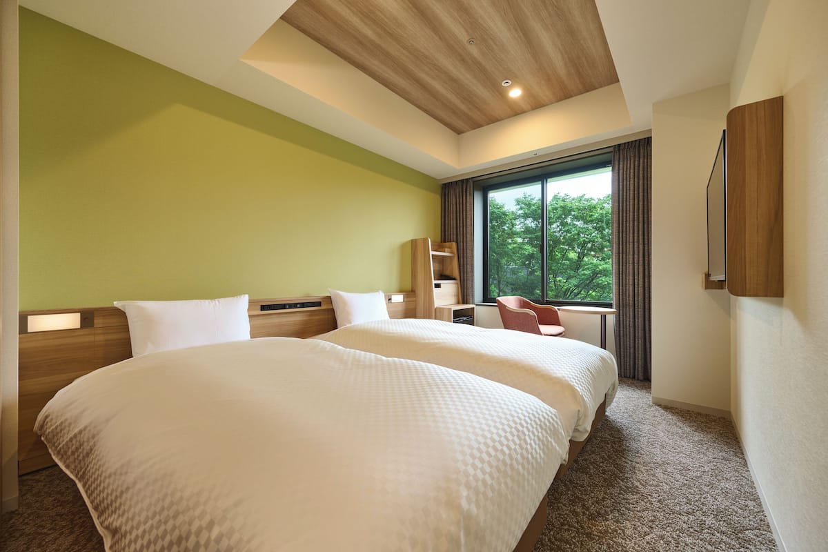 A hotel room with two beds, a large window with a view of trees, and a wooden ceiling.