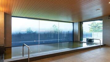 Un área de piscina interior moderna con amplios ventanales, suelo de baldosas y techo de madera.
