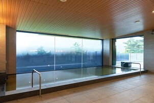 Un área de piscina interior moderna con amplios ventanales, suelo de baldosas y techo de madera.