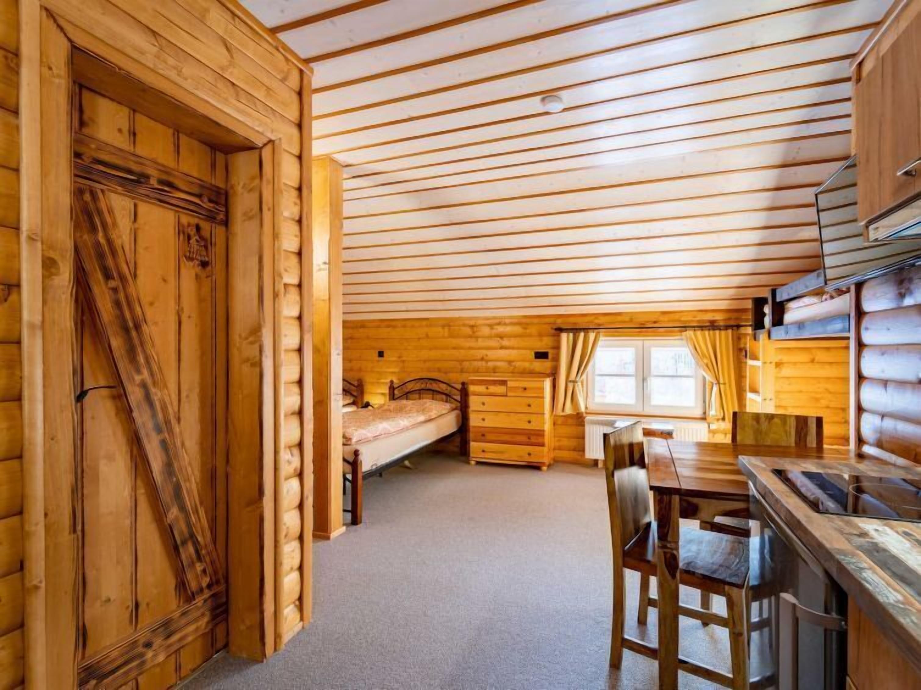 L’intérieur d’une cabane en rondins, avec un plafond en bois, un lit, une table à manger avec des chaises et un coin cuisine.
