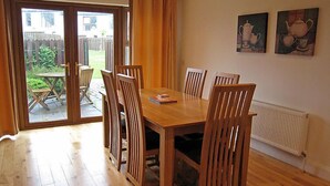 A dining area with a wooden table and chairs, a sliding glass door leading to an outdoor patio, and a radiator on the wall. - Orchard Grove by Interhome (Kenmare)