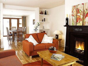 A living room with a sofa, a coffee table with magazines, a fireplace, and a dining area in the background.