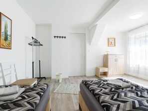 Two single beds with patterned bedding, a wardrobe, and a large window with sheer curtains.