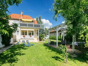 Relax on the balcony with a view of the serene surroundings, complete with a well-maintained lawn and a shaded pergola.