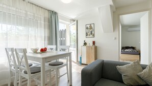 A modern living room with a grey sofa and white dining table, a small cabinet, and a bed in the background. - Meretei Porta by Interhome (Balatonkeresztur)