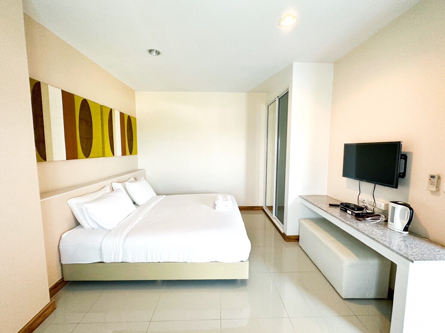 A modern hotel room with a large bed, a flat-screen TV, a coffee maker, and a desk.