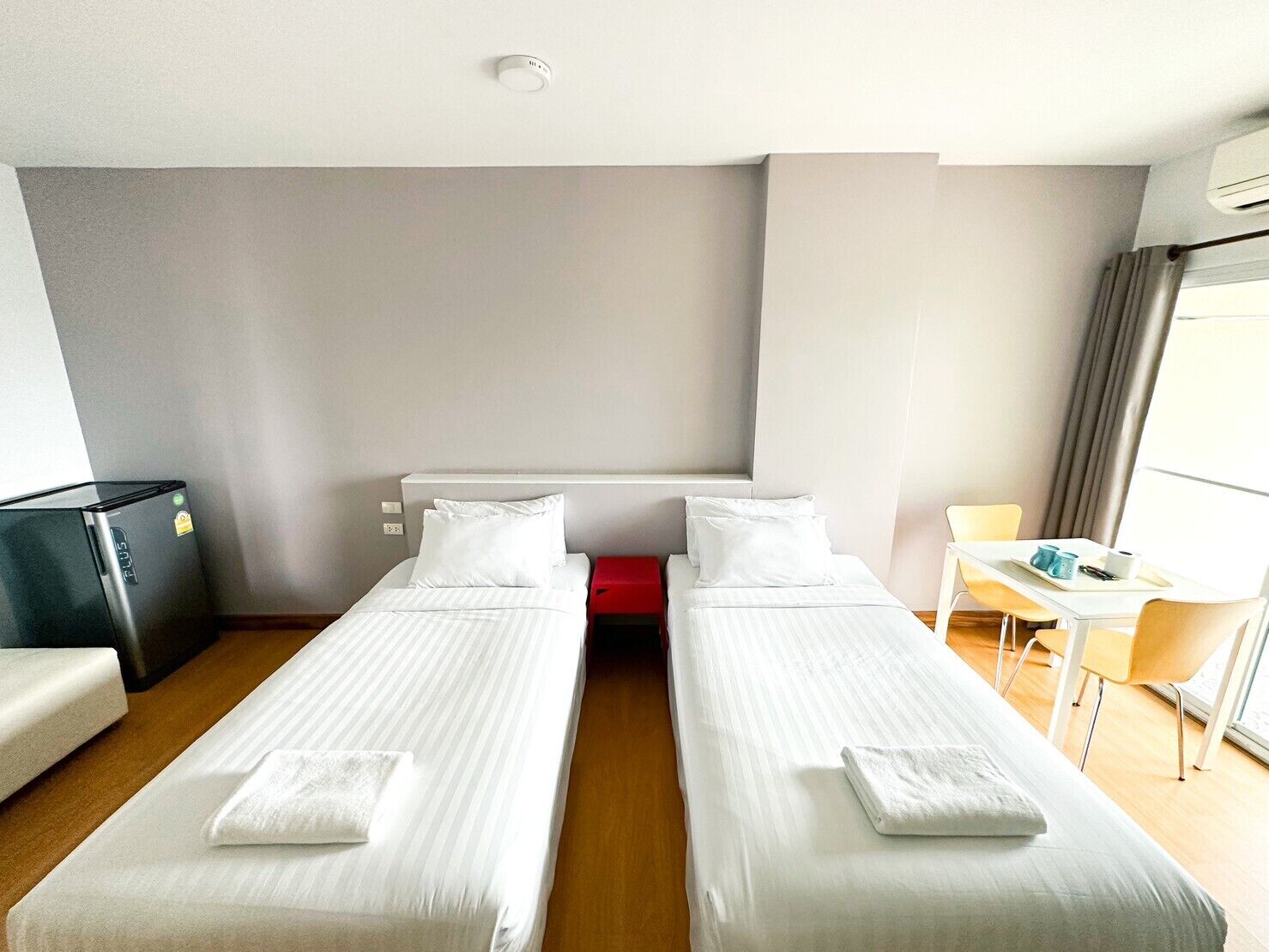 Una habitación de hotel con dos camas individuales, un escritorio pequeño, una silla y un minibar.