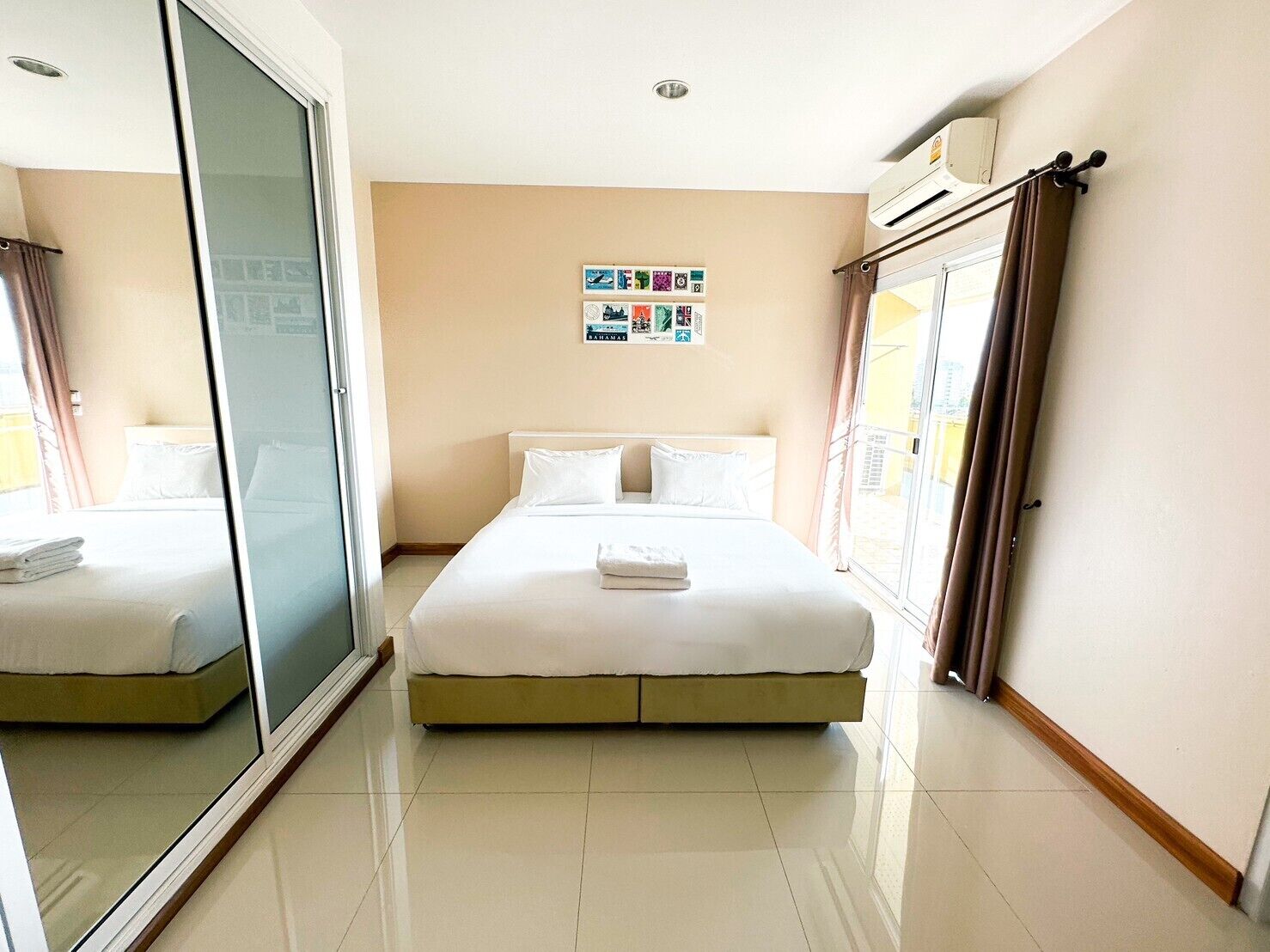 A hotel room with a bed, a sliding glass door, a wall with a photo collage, and a window with curtains.
