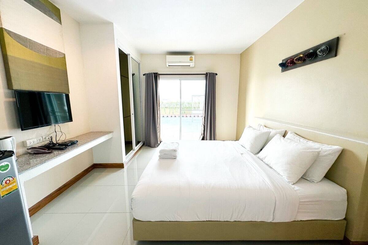 A hotel room with a bed, a TV on a stand, a desk with a computer and a phone, and a window with curtains.